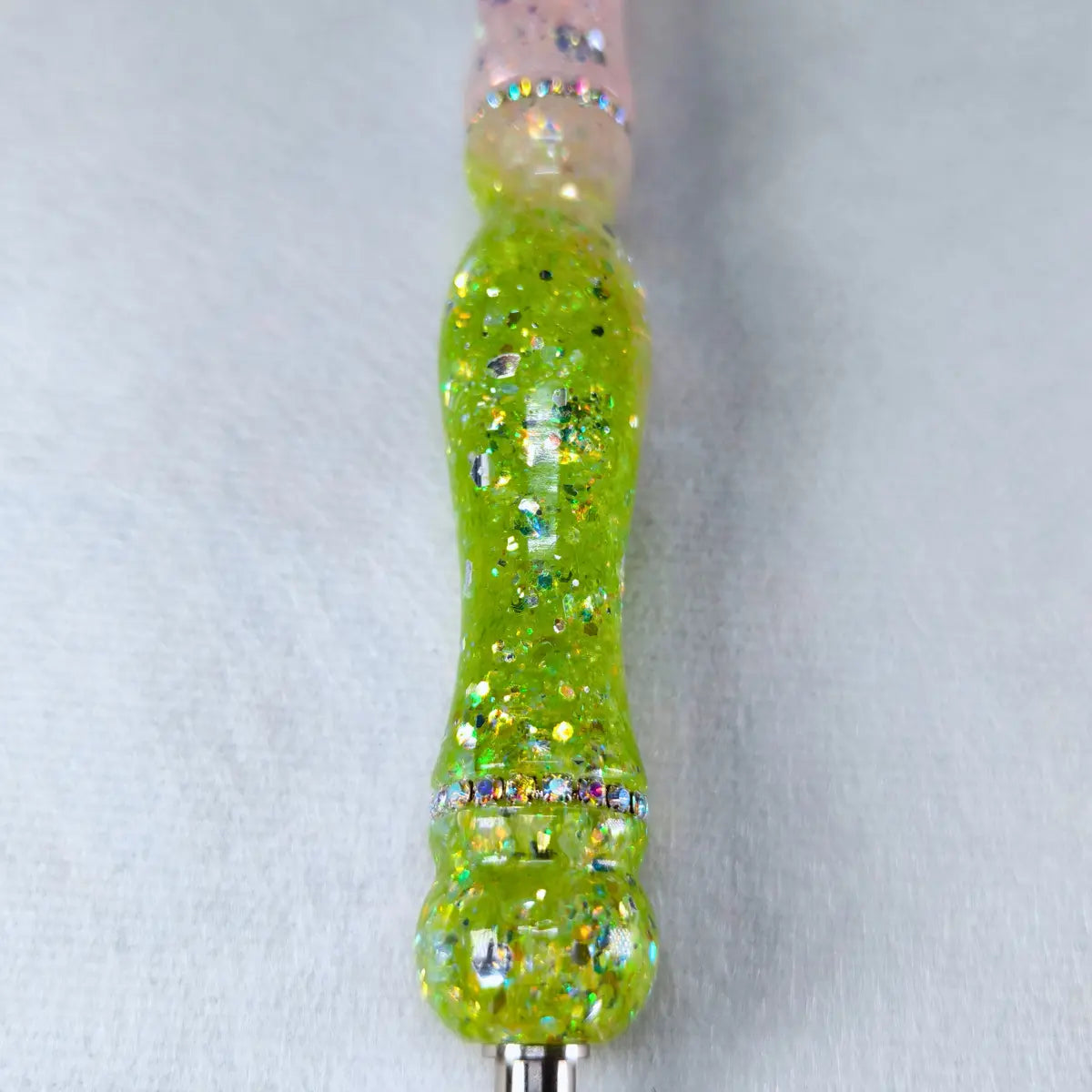 Gros plan sur le manche rose clair et vert pailleté du stylet fait main