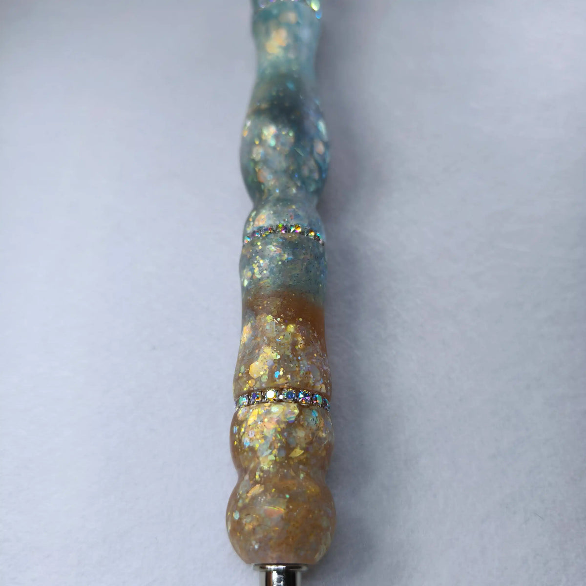 Gros plan sur la transition ambre et bleu glacier satinée avec bague sertie de strass brillants et éclats dorés.