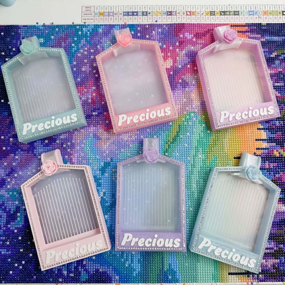 Assortiment de plateaux de tri pour broderie diamant aux couleurs pastel (bleu, rose, violet) posés sur une toile de travail.