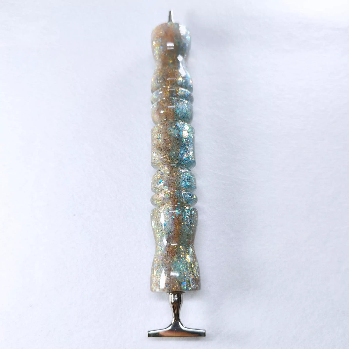 Stylo ergonomique en résine à finition brillante avec dégradé sable doré et bleu lagon parsemé de paillettes scintillantes.