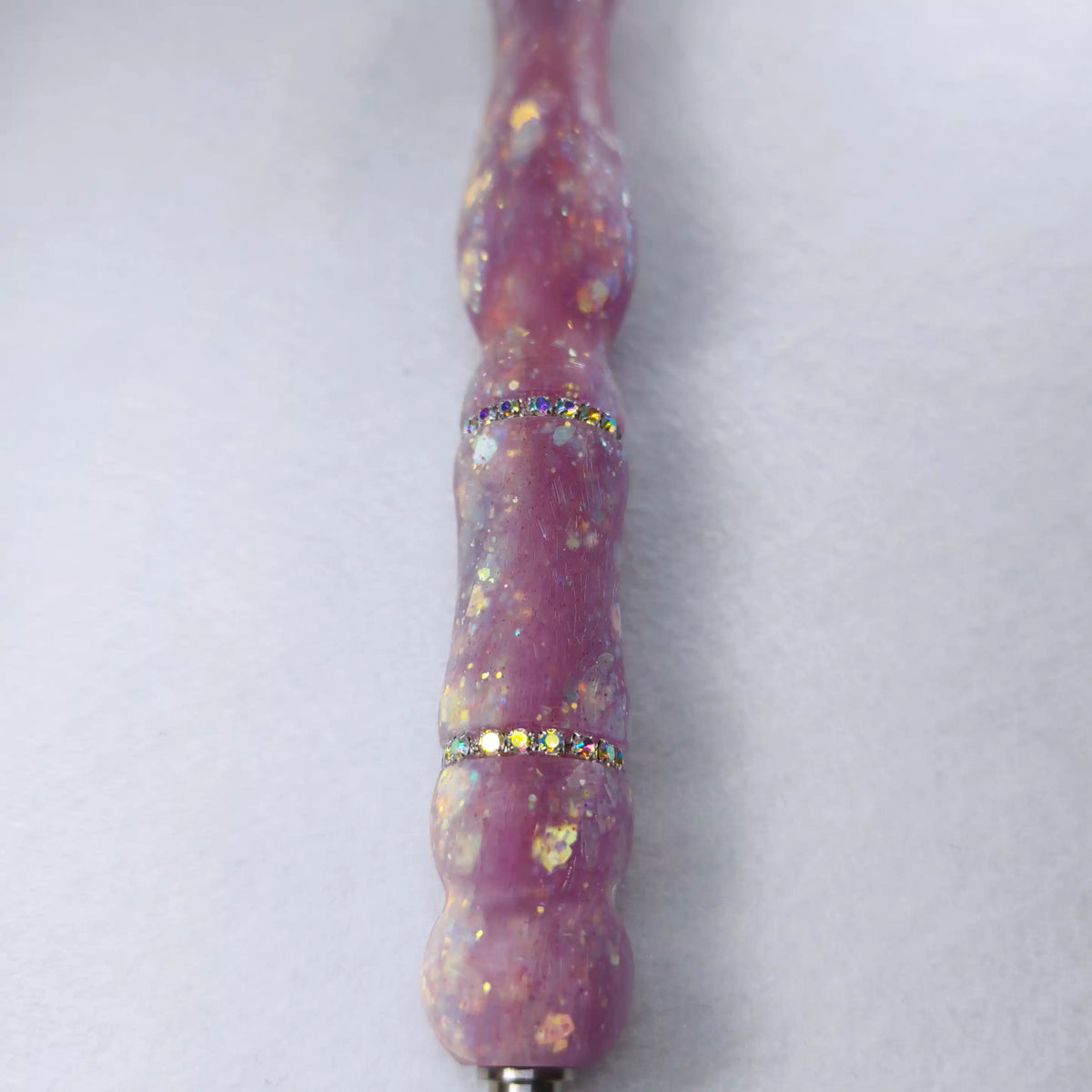 Détail de la surface satinée mate lilas avec paillettes dorées fines et deux bagues de strass étincelants.
