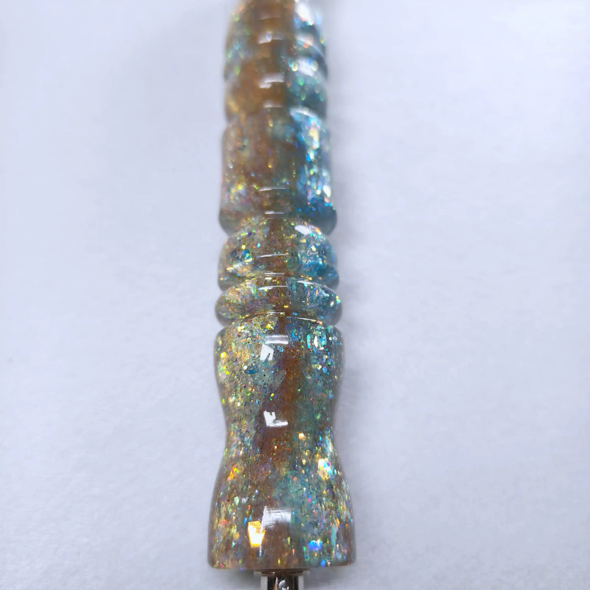 Gros plan sur la résine brillante du stylo Lagune Dorée montrant le dégradé sable chaud et bleu lagon incrusté de paillettes scintillantes.